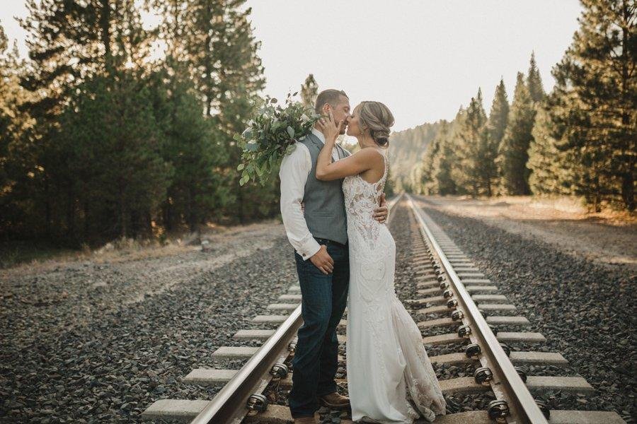Danielle and Scott kiss on the railroad tracks among the pines, photo by Composing Reality Photography