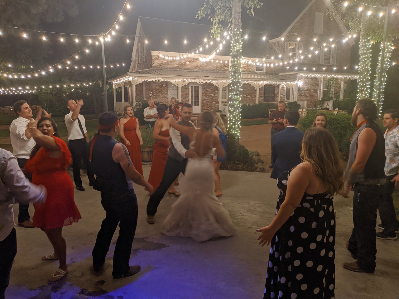 Danielle and Scott dance in a circle of guests under the string lights late at night