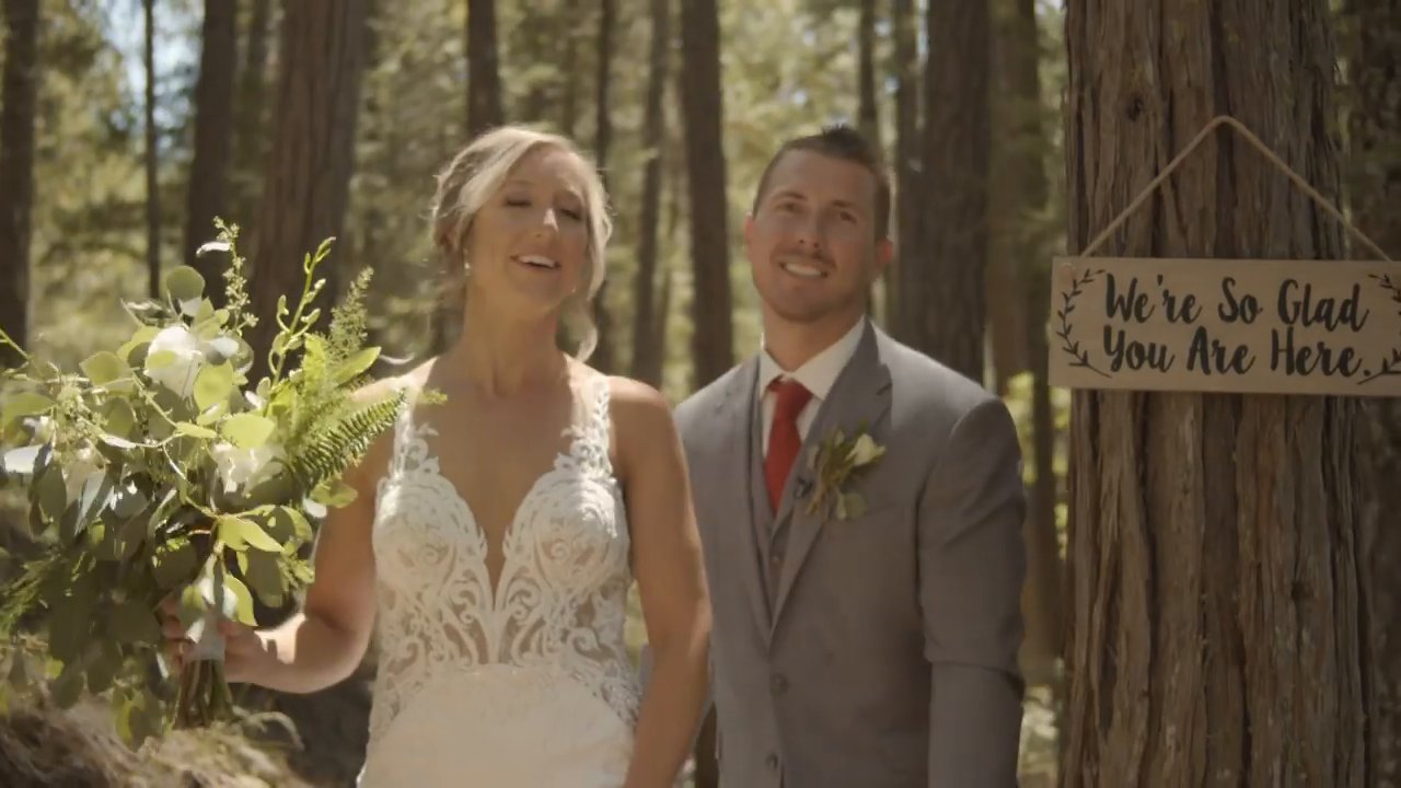 Danielle and Scott laugh together beside the We're So Glad You Are Here sign.