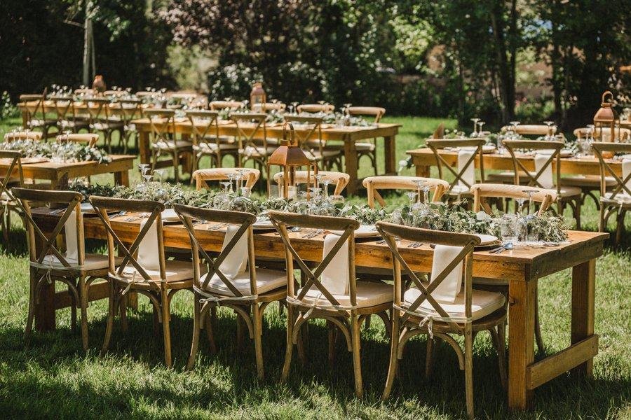 Long wooden tables with cross back chairs set on the lawn, photo by Composing Reality Photography