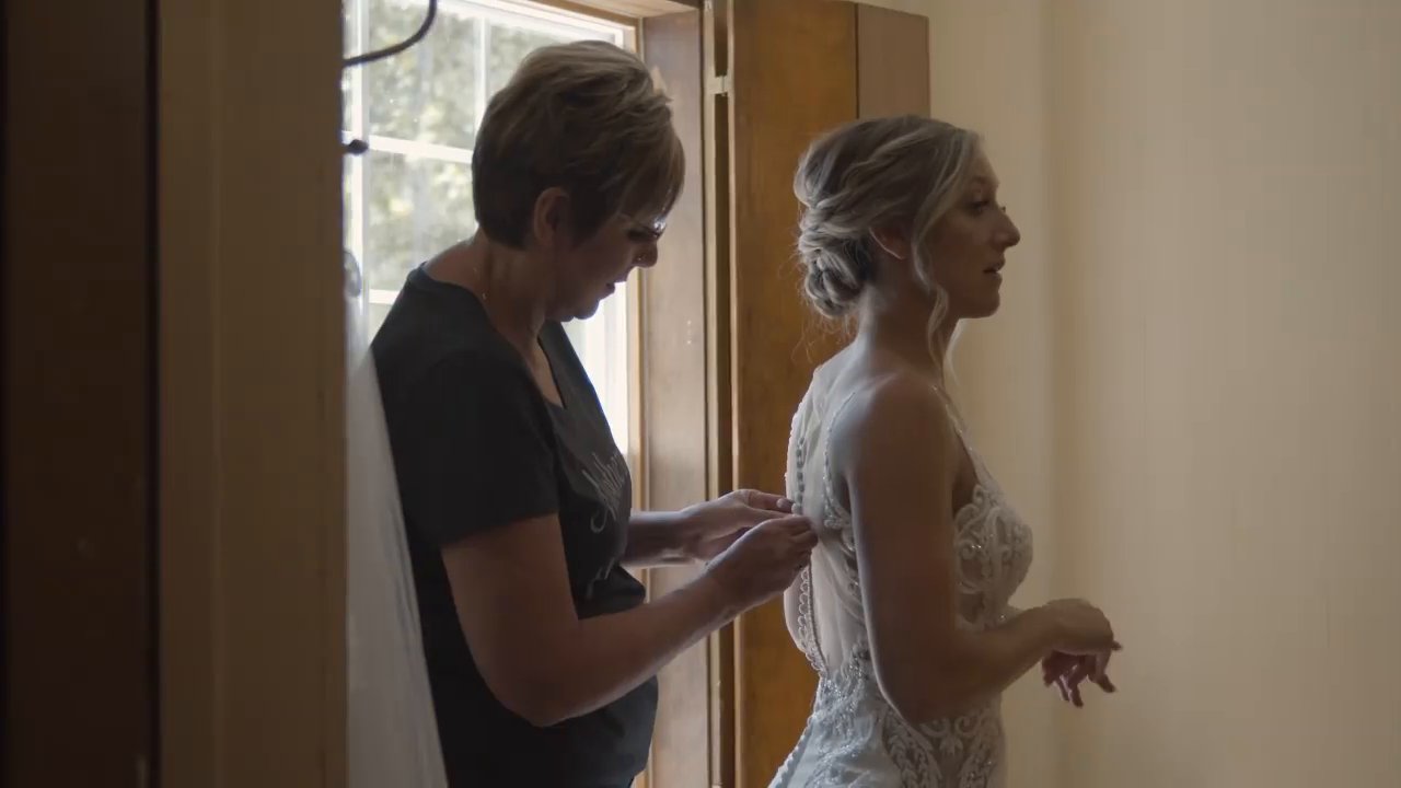 Danielle's mom buttons the back of her gown by the window.