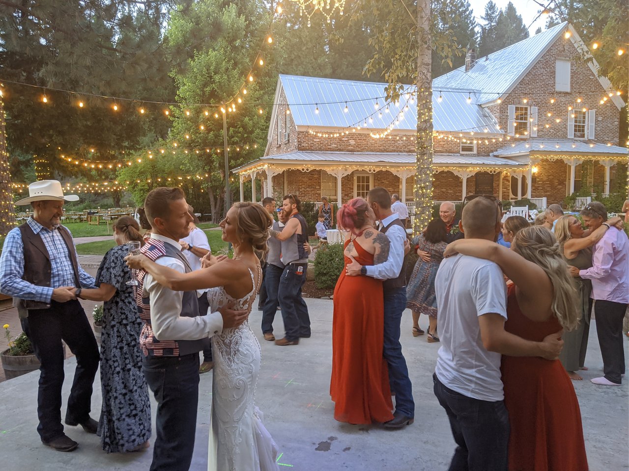 Danielle and Scott slow dance with their guests under string lights in front of the brick house