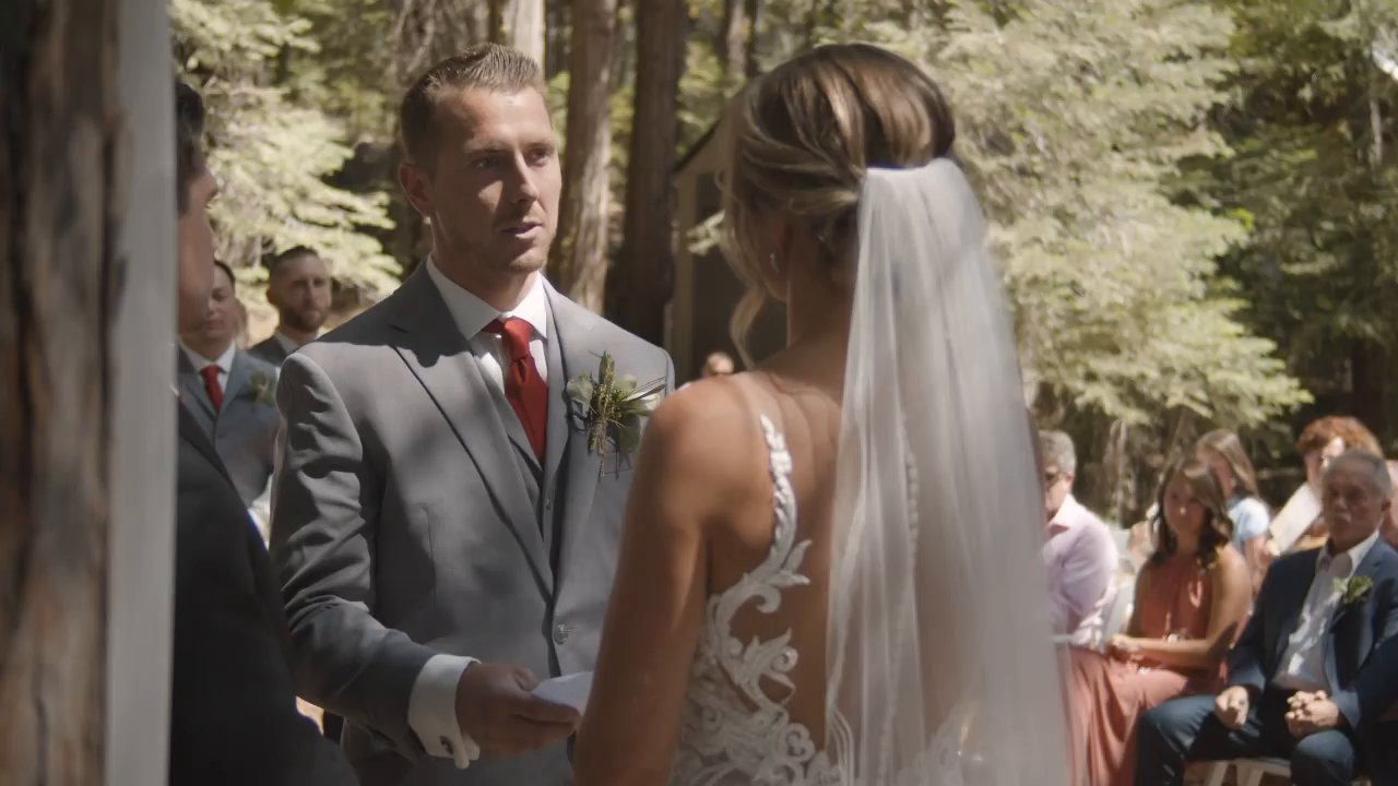Scott reads his vows to Danielle at the arch as guests watch from the forest seats.