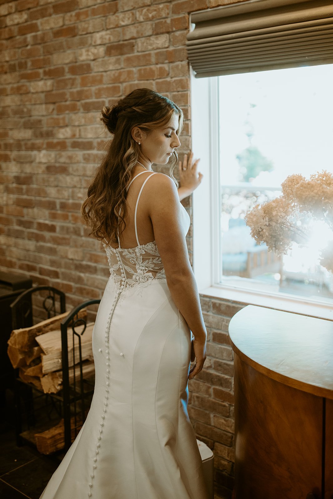 Emily looks out the window in her gown, the buttons down her back
