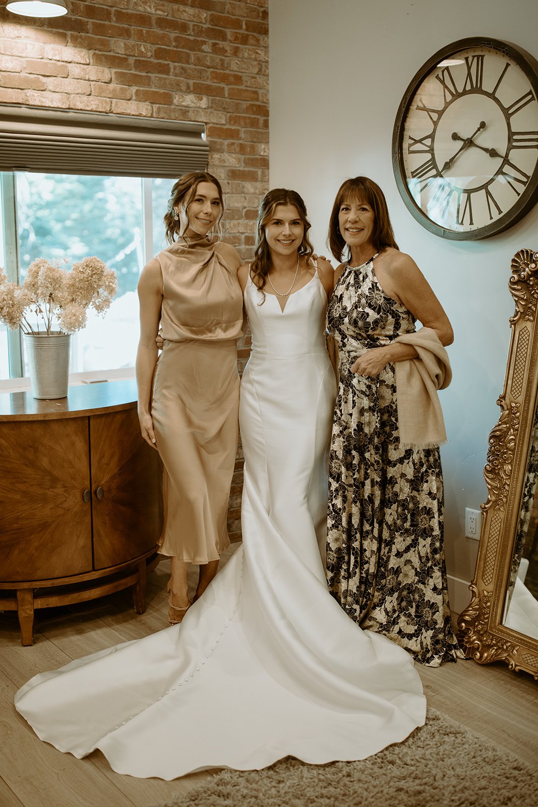 Emily in her gown between two loved ones by the gold mirror