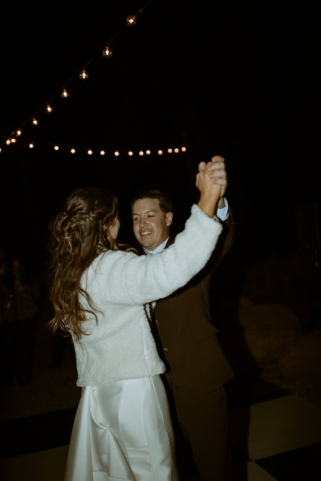 Devin twirls Emily under the string lights