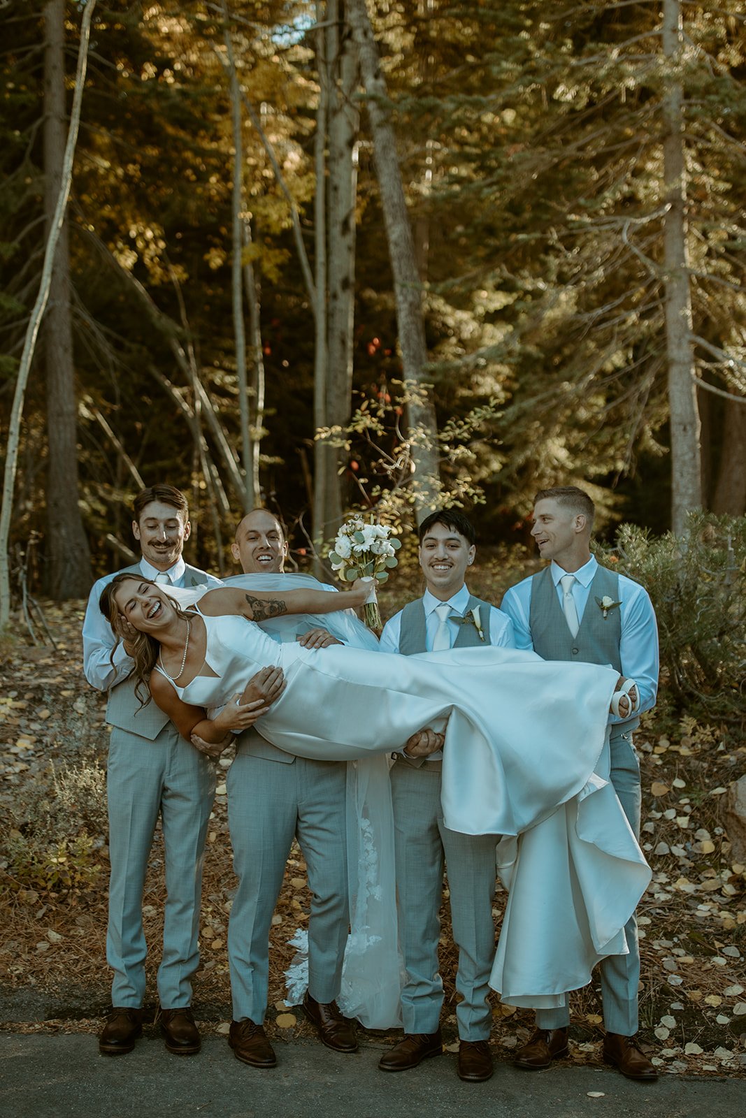 The groomsmen hold Emily across their arms in the aspens