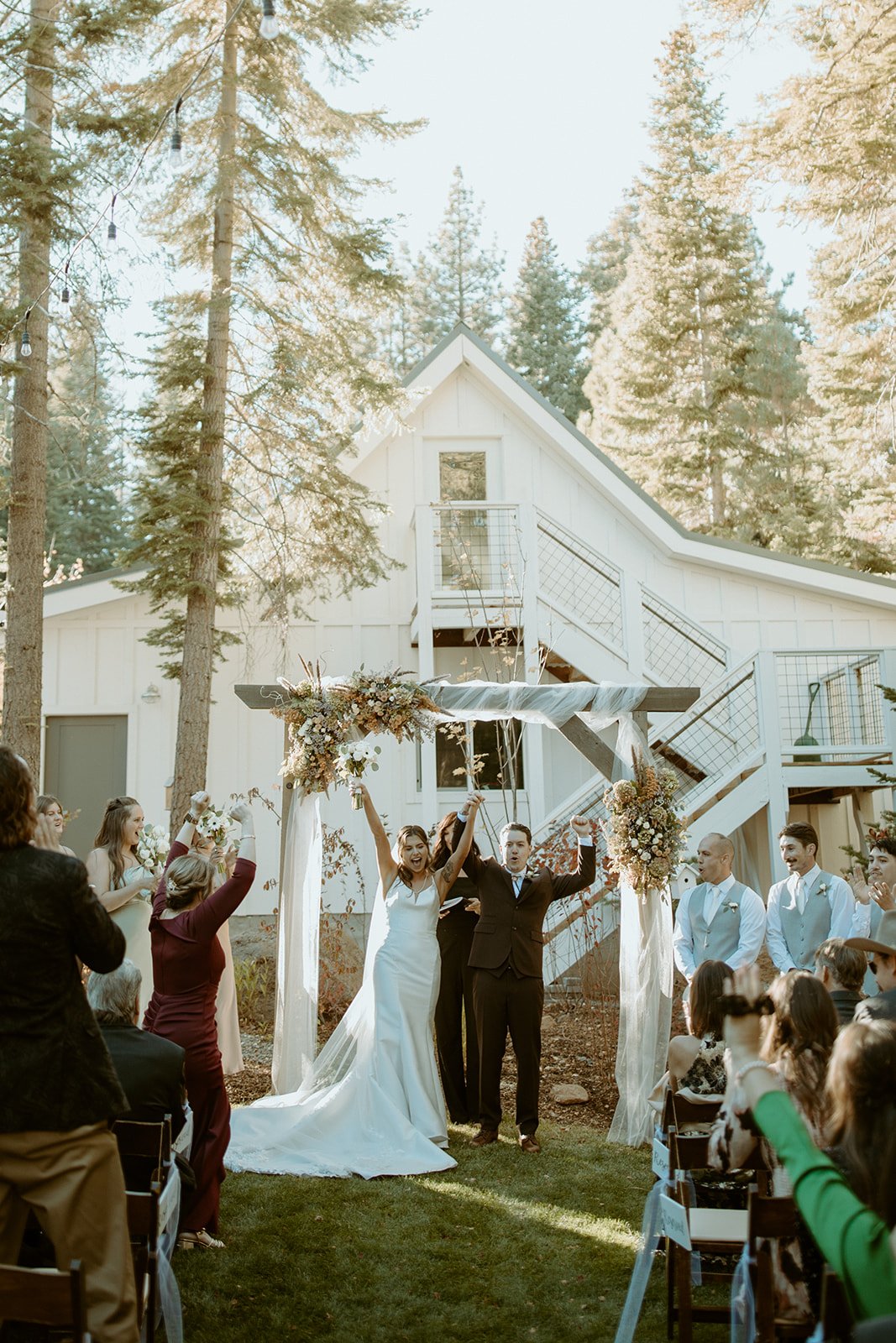 Emily and Devin raise their arms as guests cheer at the arch
