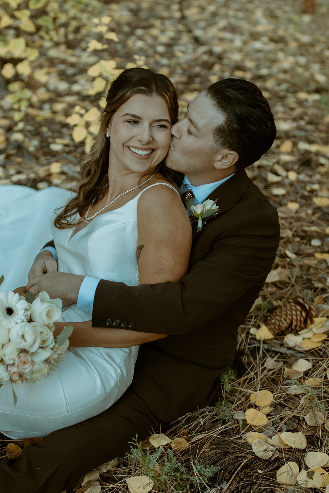 Devin kisses Emily's cheek as they sit in the golden leaves