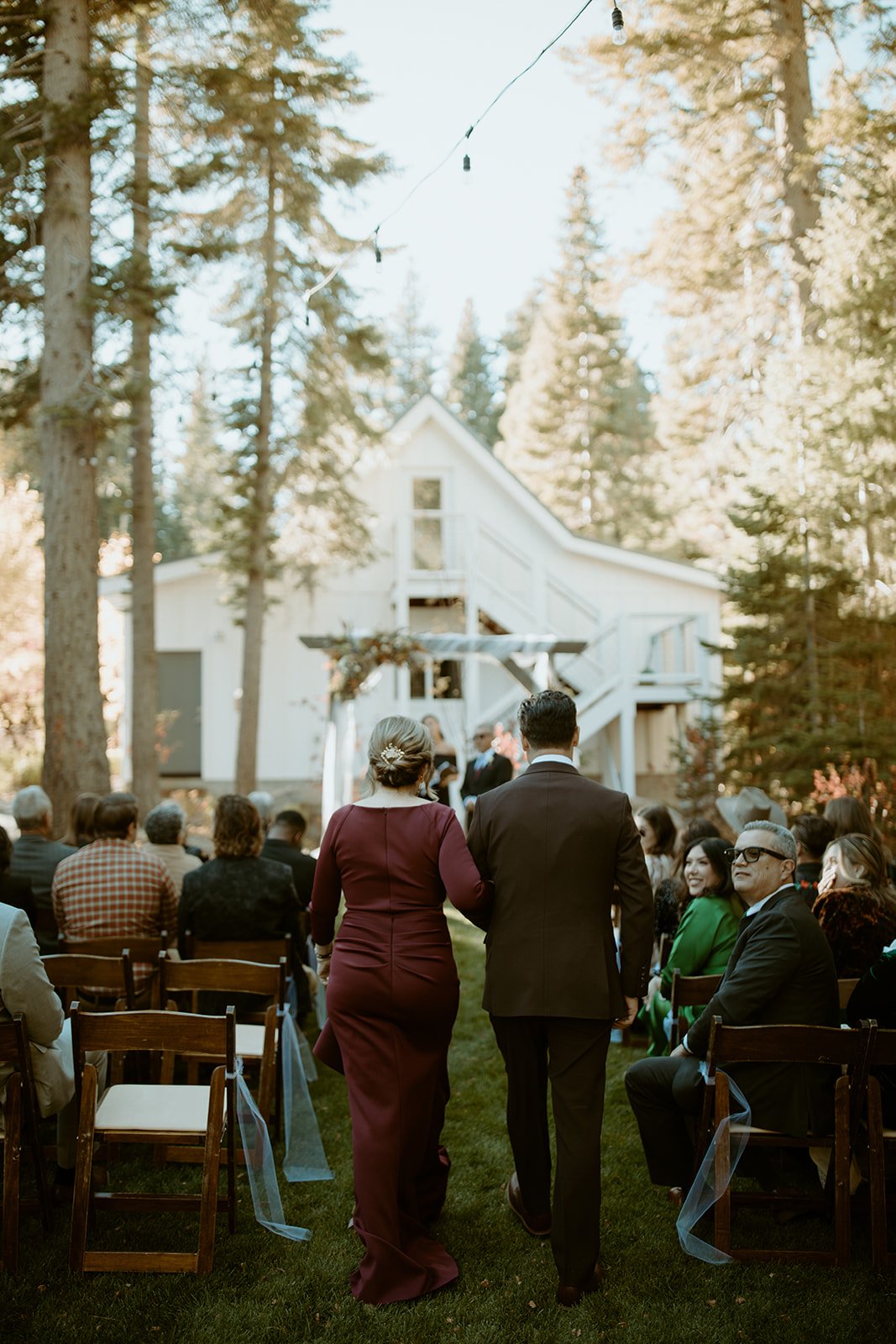 Family walks down the aisle toward the white house in the pines