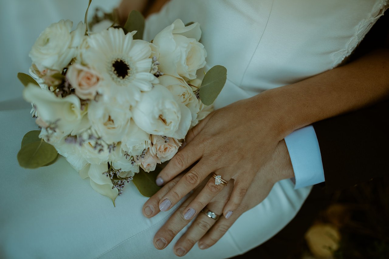 Emily's hand with her rings over her white bouquet