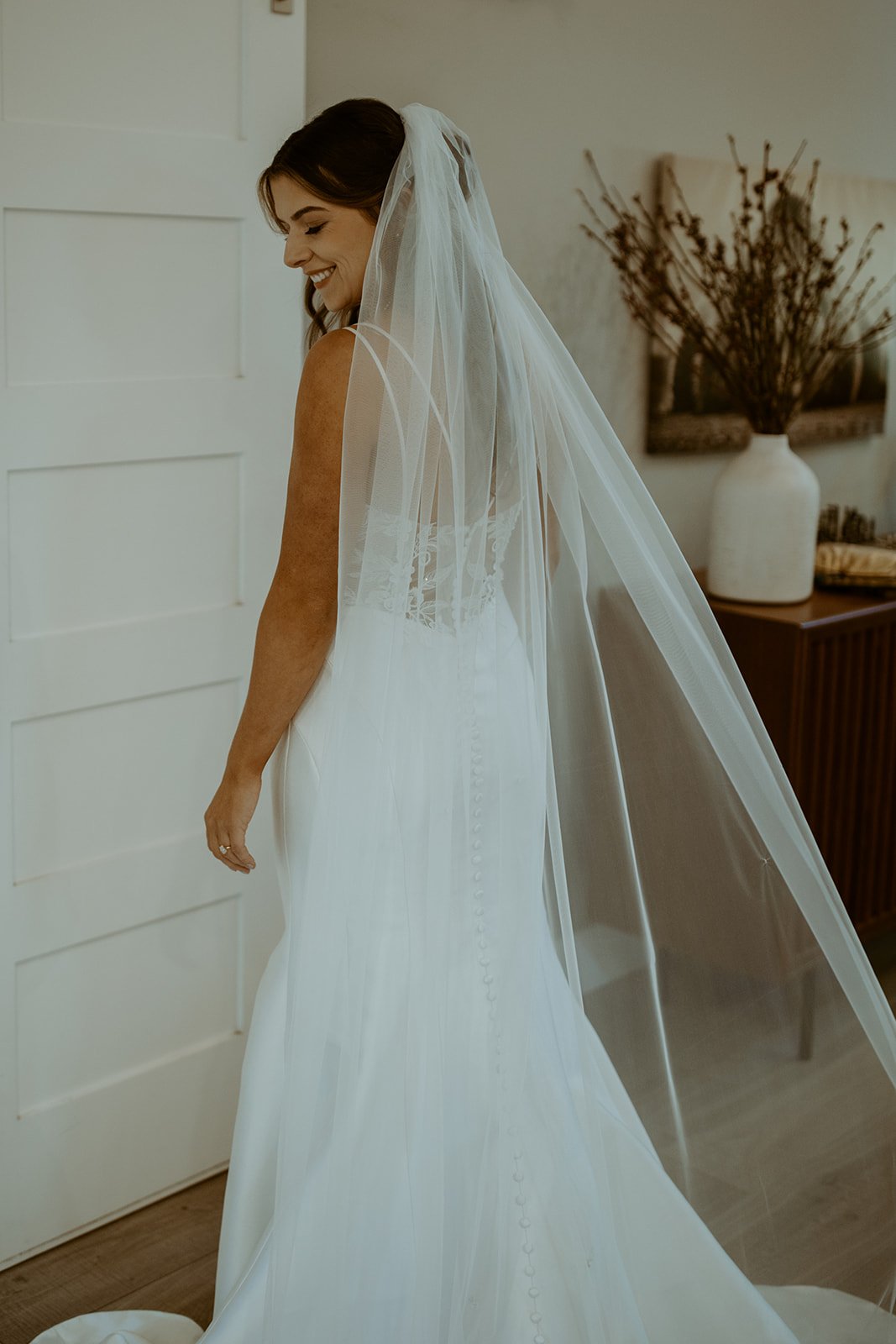 Emily smiles over her shoulder under her long veil