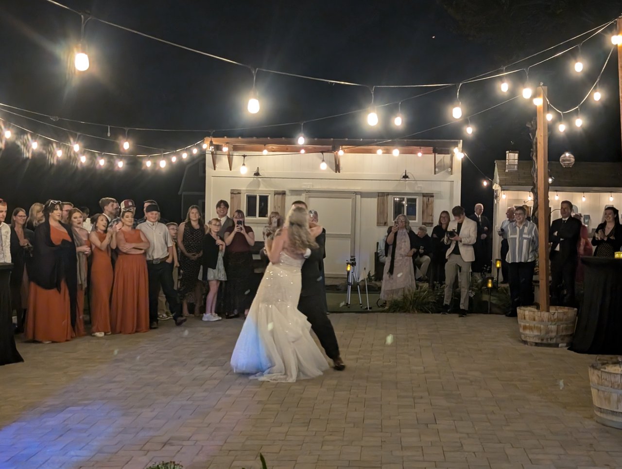 Emily and Logan hold each other close during their first dance, the bridesmaids in rust gowns behind them
