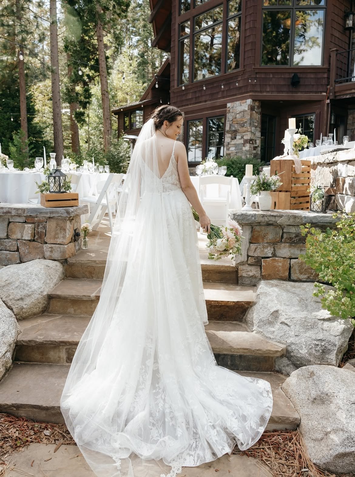 Emma stands on the stone steps in her long veil, facing the house and the set tables
