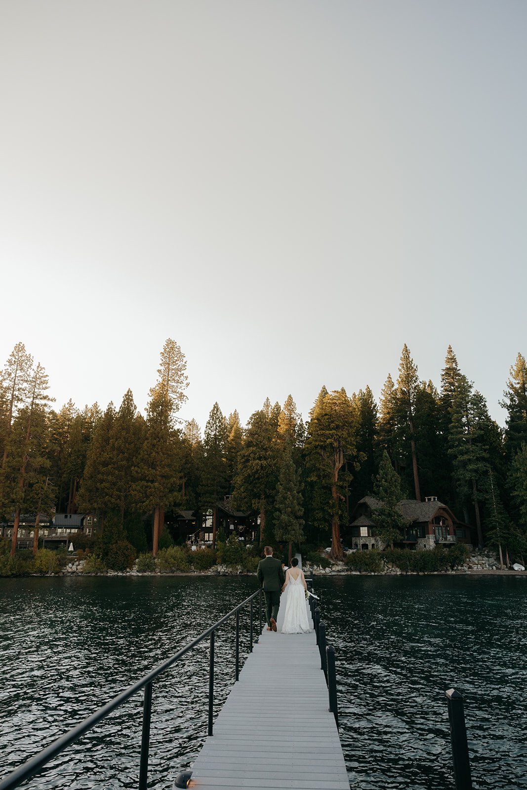 Emma and Jackson stand at the far end of the long pier under the tall pines