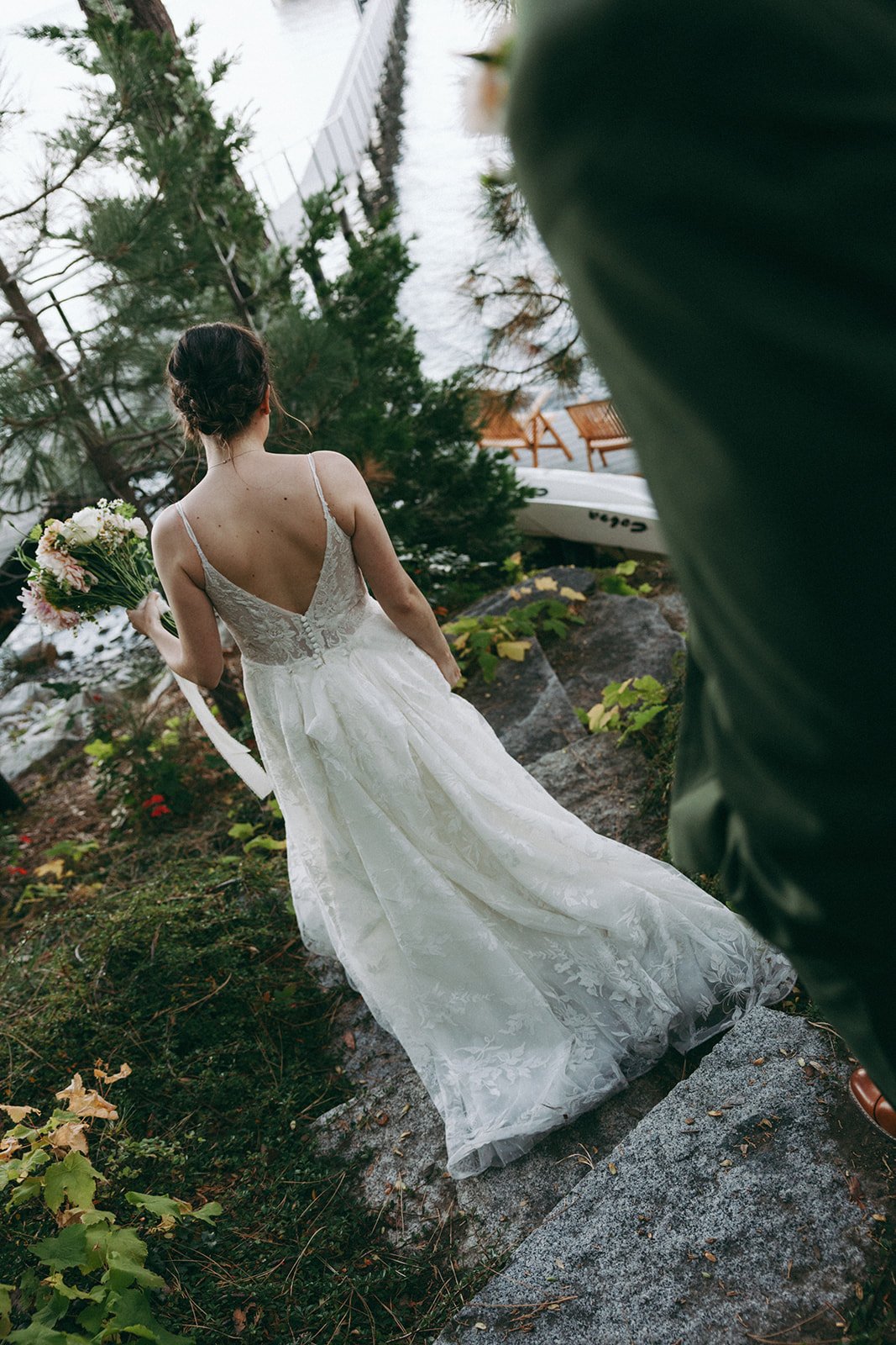 Emma steps down the rocks toward the water, her dress trailing behind her