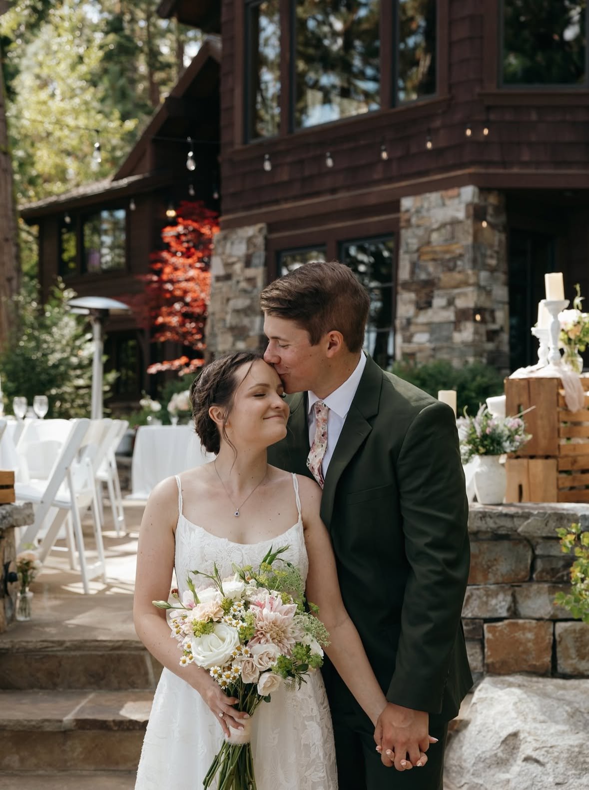 Jackson kisses Emma on the forehead by the stone terrace, her bouquet of blush flowers in hand