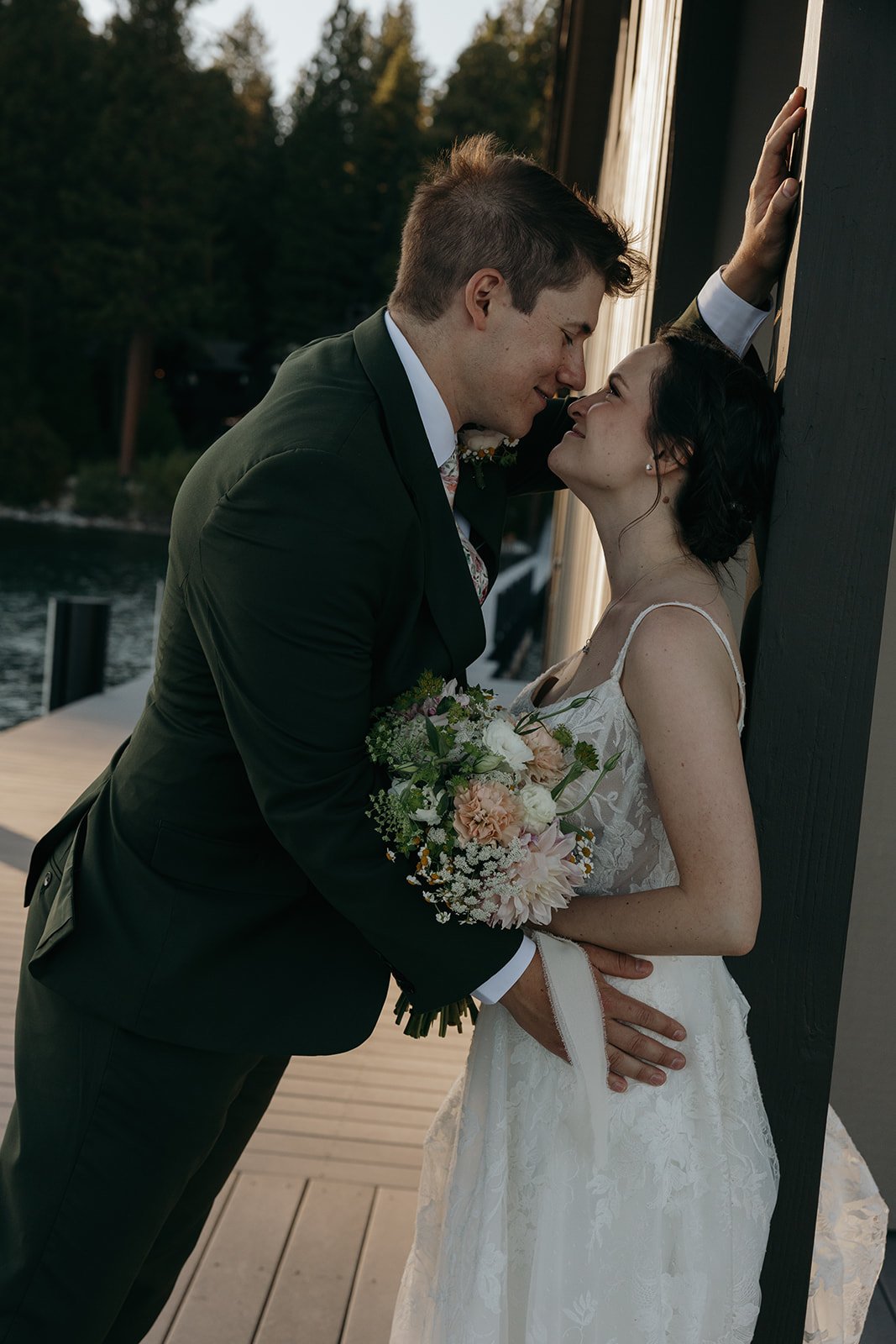 Jackson leans in for a kiss as Emma rests against the boathouse