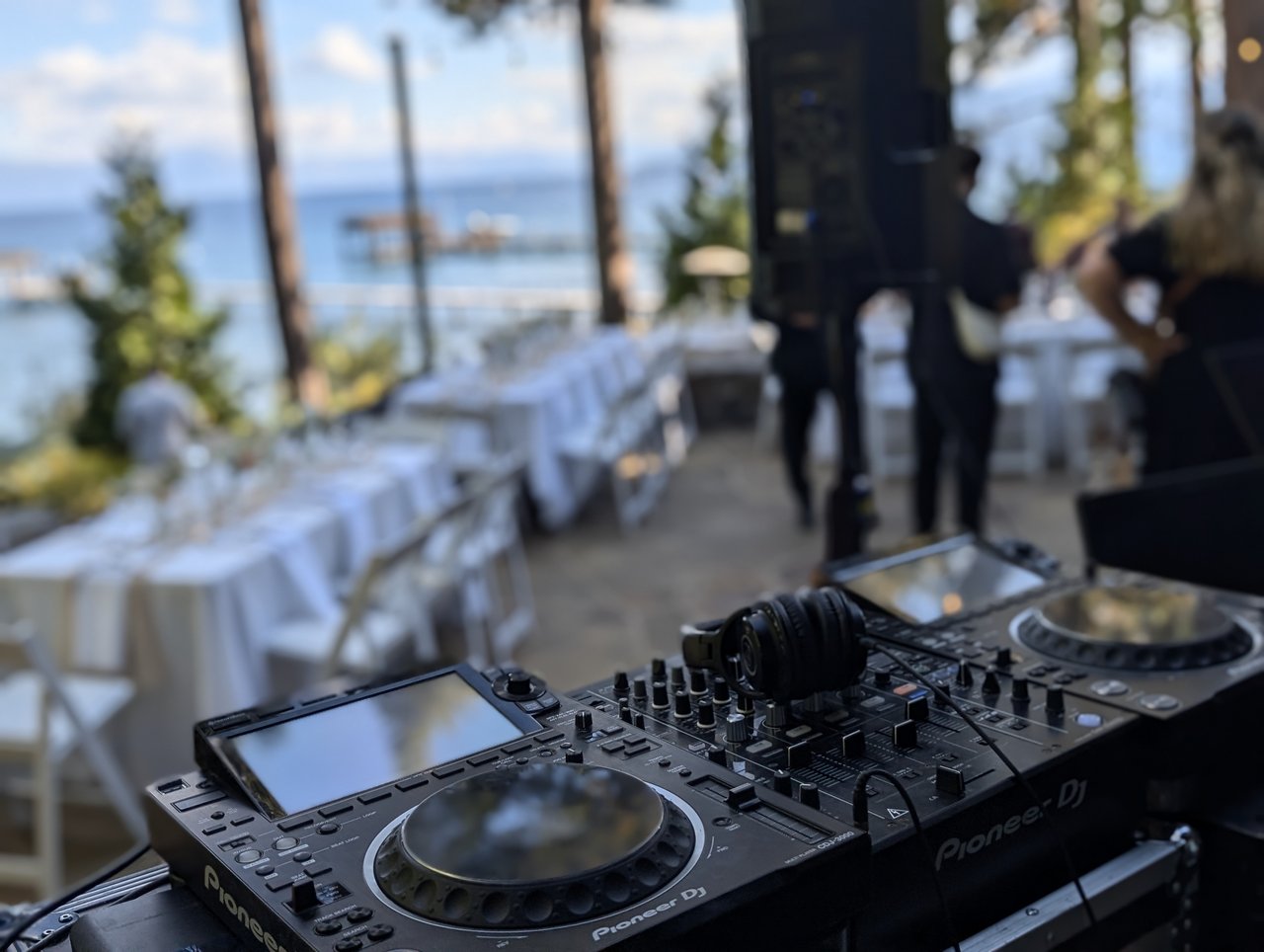 A close view of the Pioneer DJ decks with the reception tables and the lake behind them