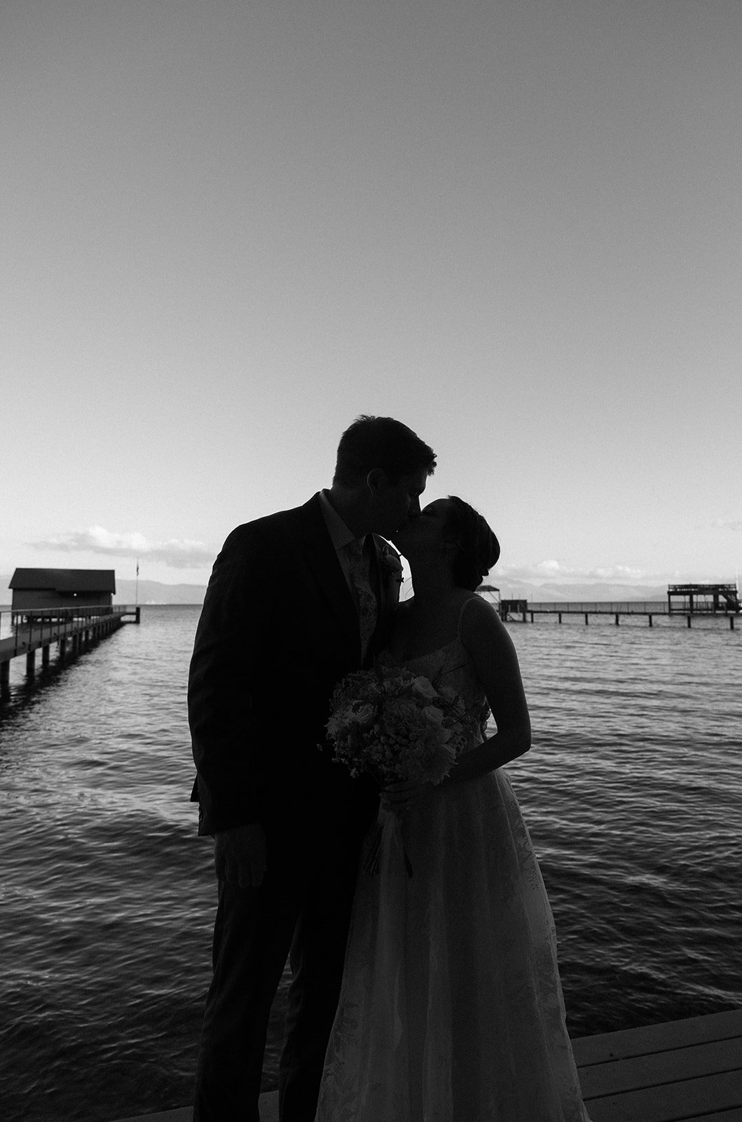 Emma and Jackson kiss in silhouette on the pier, in black and white