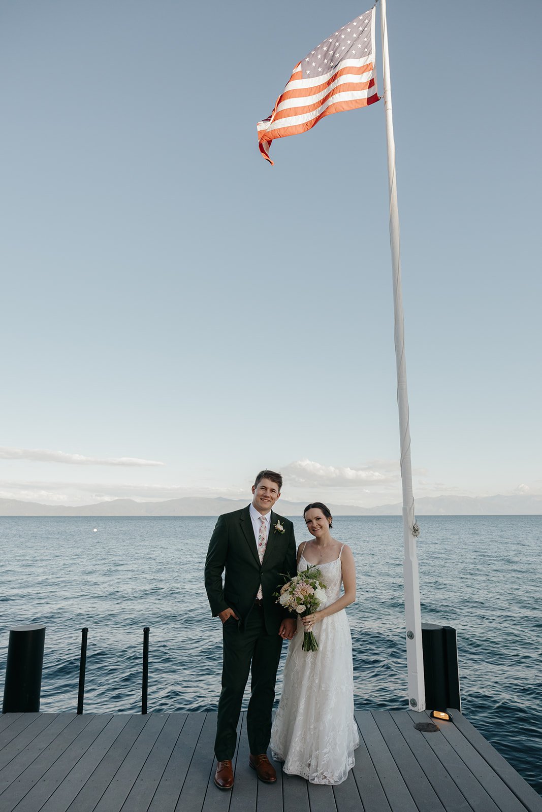 Emma and Jackson stand together under the flag at the end of the pier, the lake all around