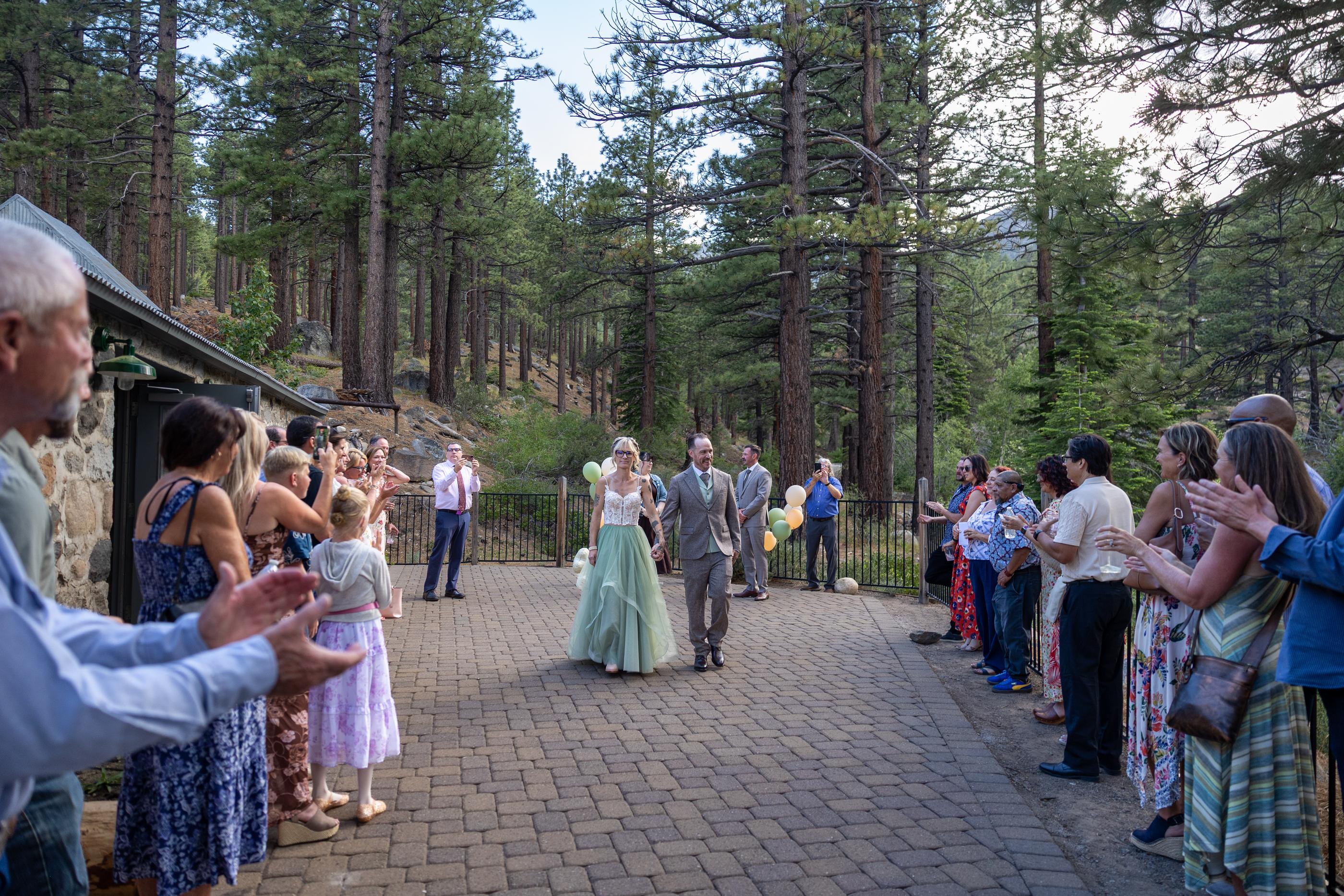 Guests cheer as Amy and Justin walk back up the aisle beside the stone Galena Creek Fish Hatchery building in the pines