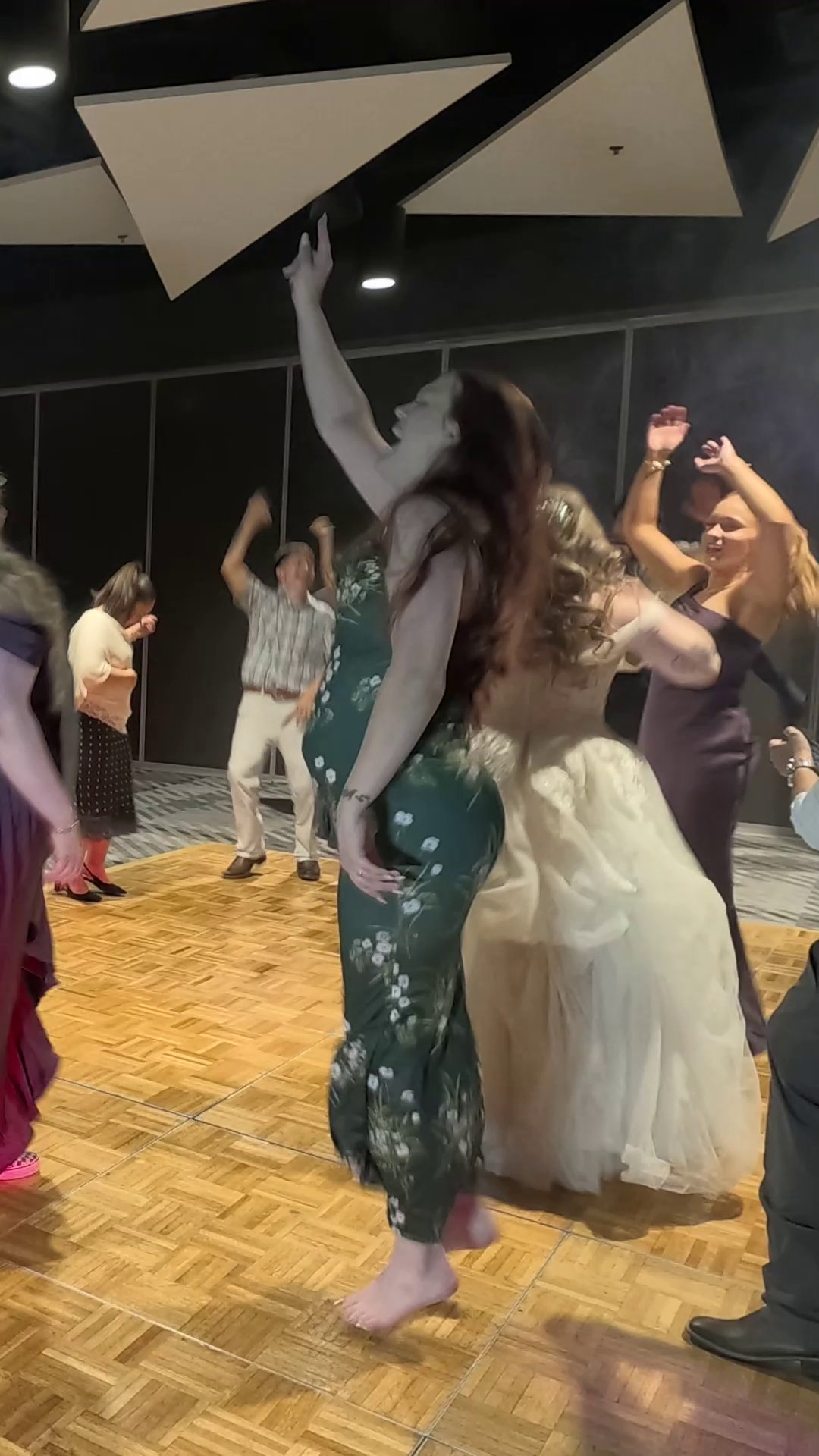 Hailey dances with her bridesmaids, one with her arm raised high, on the wooden dance floor in the Topaz Room