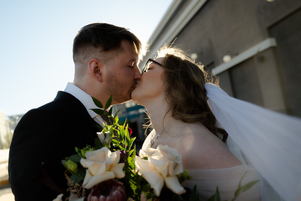 Hailey and Zen kiss in the sunlight over her bouquet