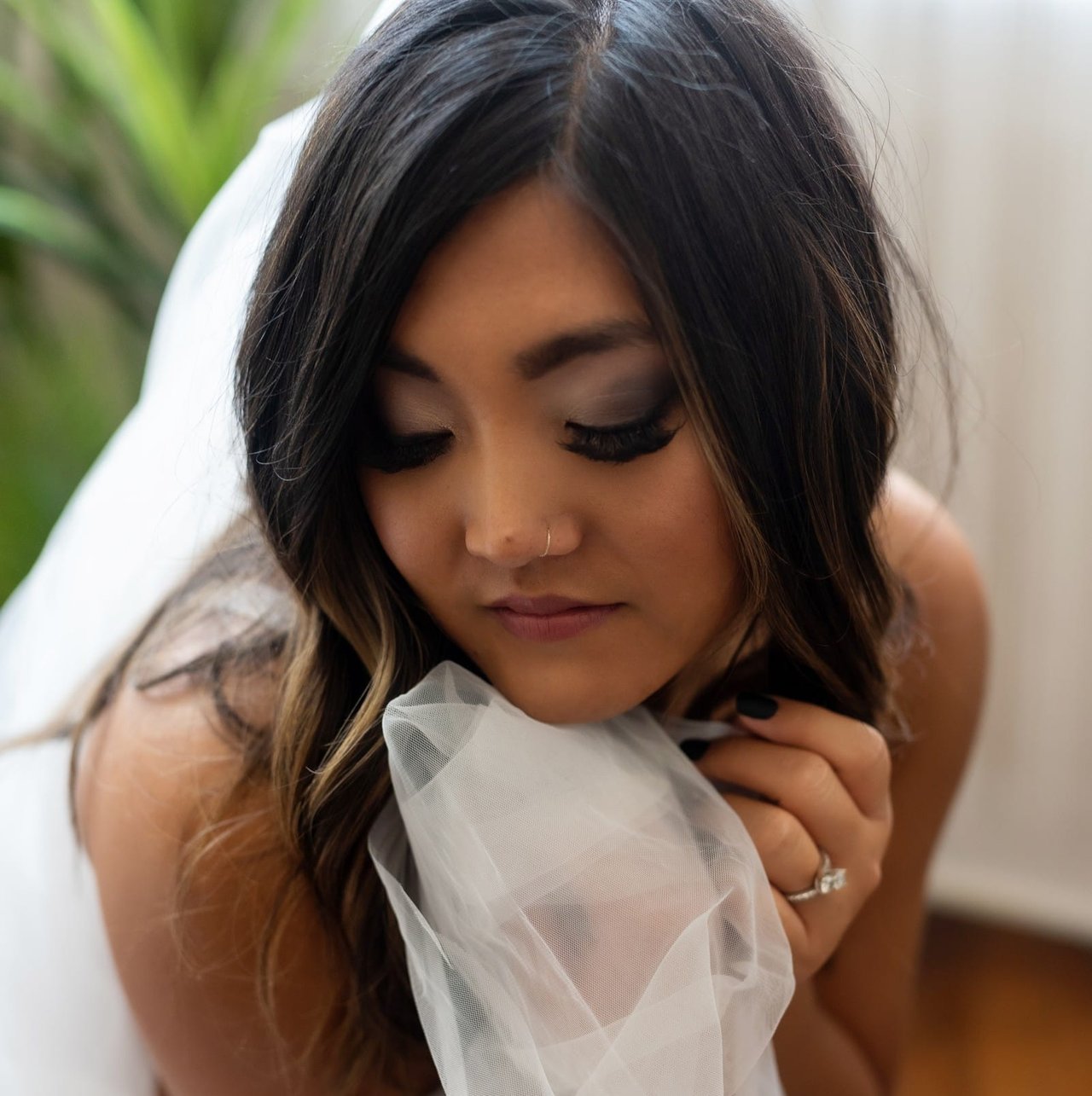 Hannah holds her veil to her cheek, eyes lowered, her engagement ring on her hand