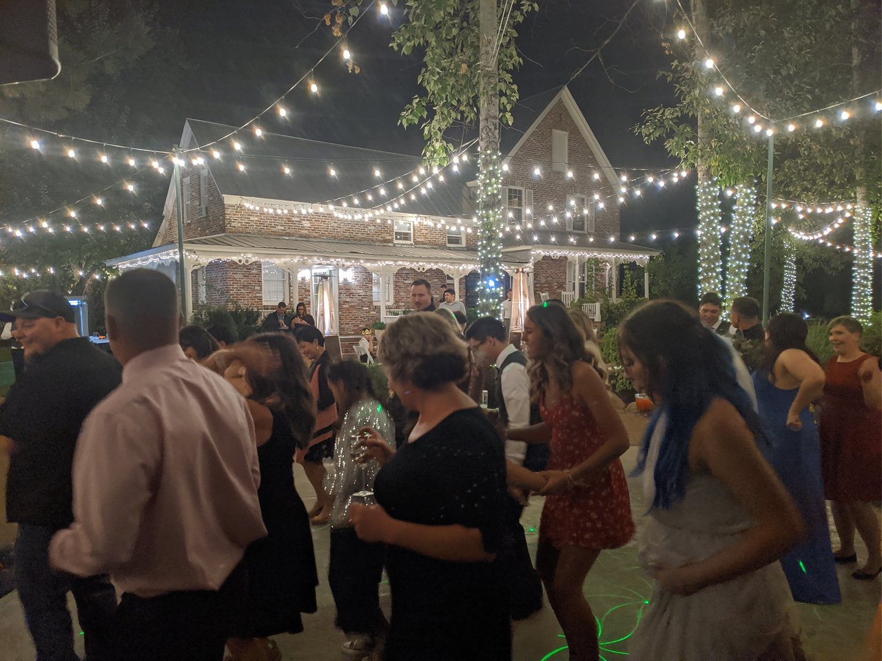 Guests dance under the string lights in front of the brick house at Twenty Mile House