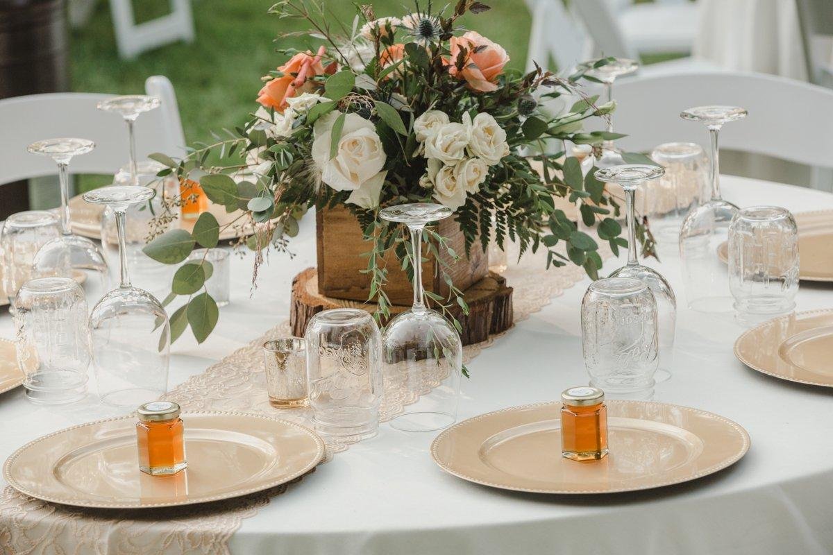 A round table with a rose centerpiece and honey jar favors on gold chargers