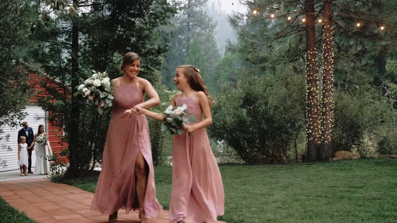 Two bridesmaids in blush dresses dance their way into the reception across the lawn