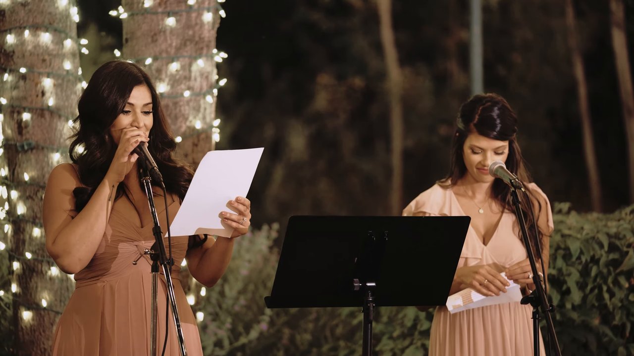 Two bridesmaids give their toast under the string lights