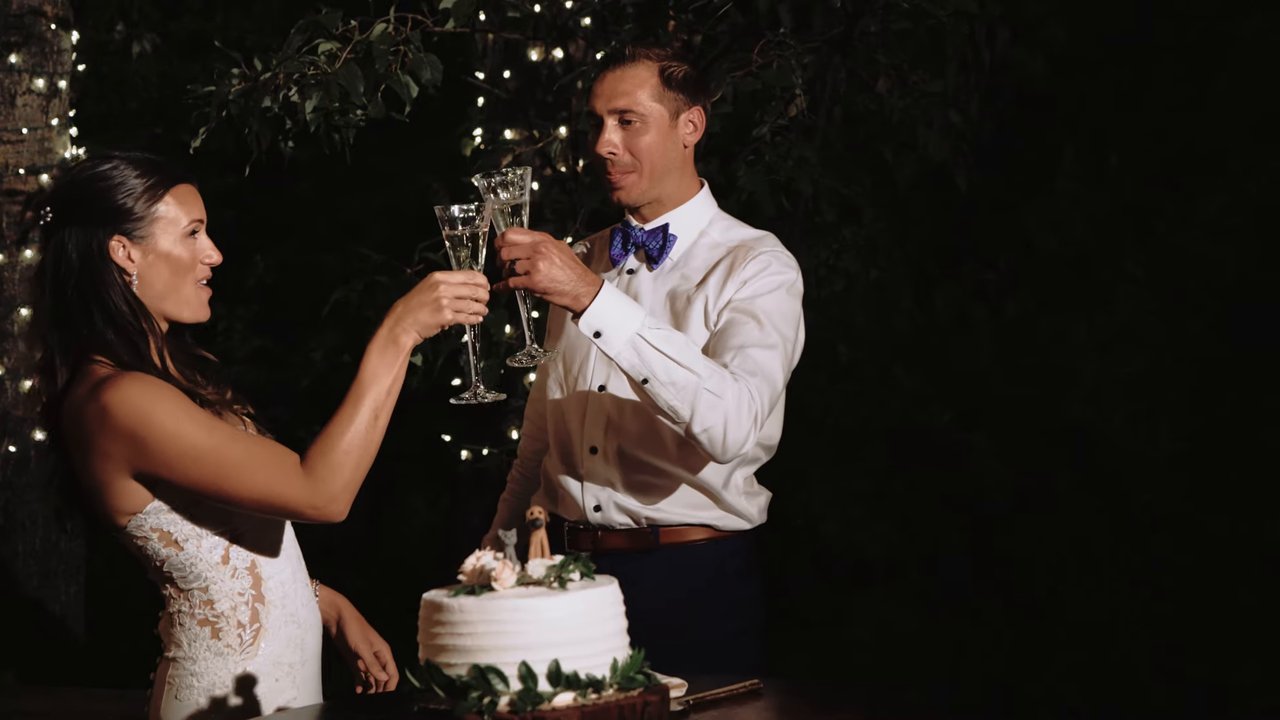 Jen and Wes clink champagne glasses at the cake