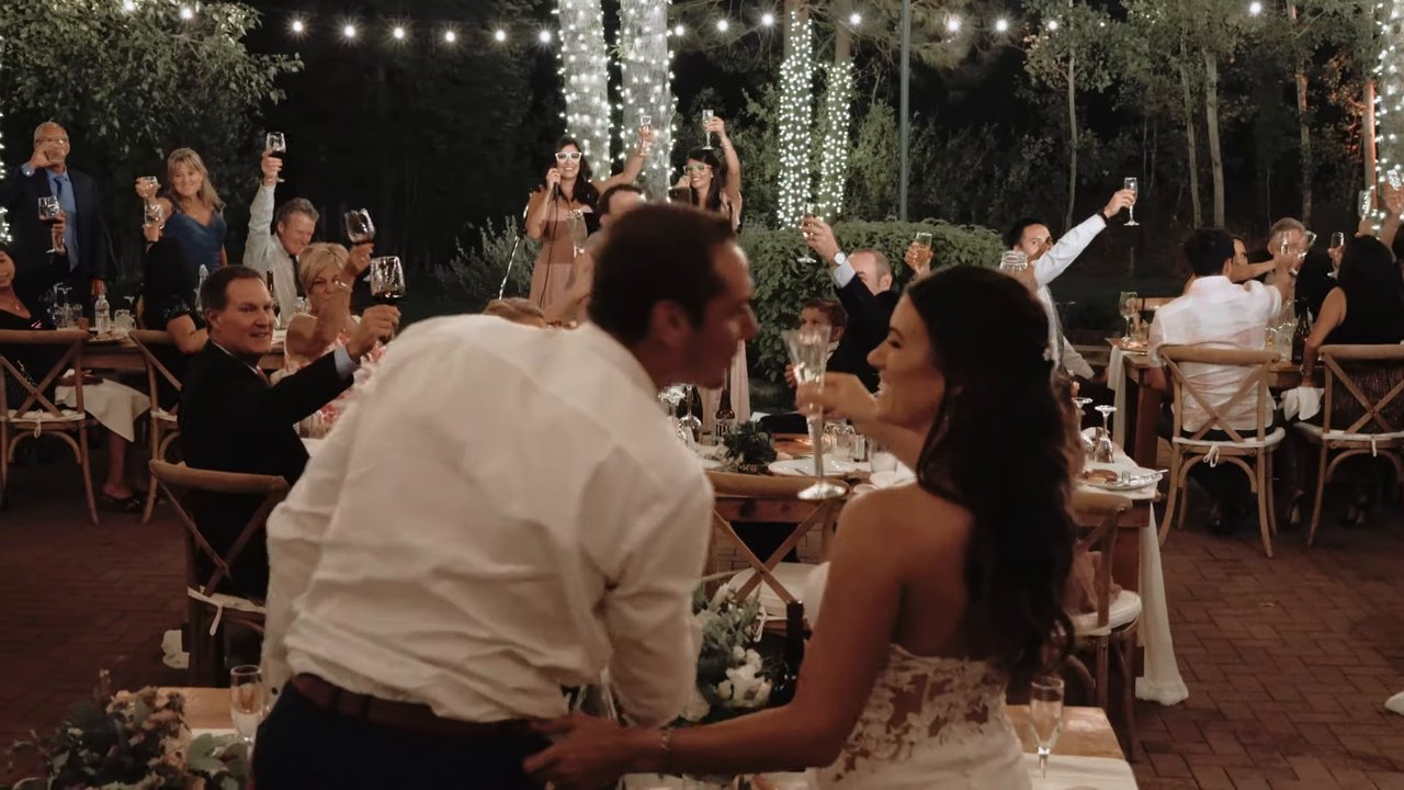 Jen and Wes stand at their table as guests raise their glasses
