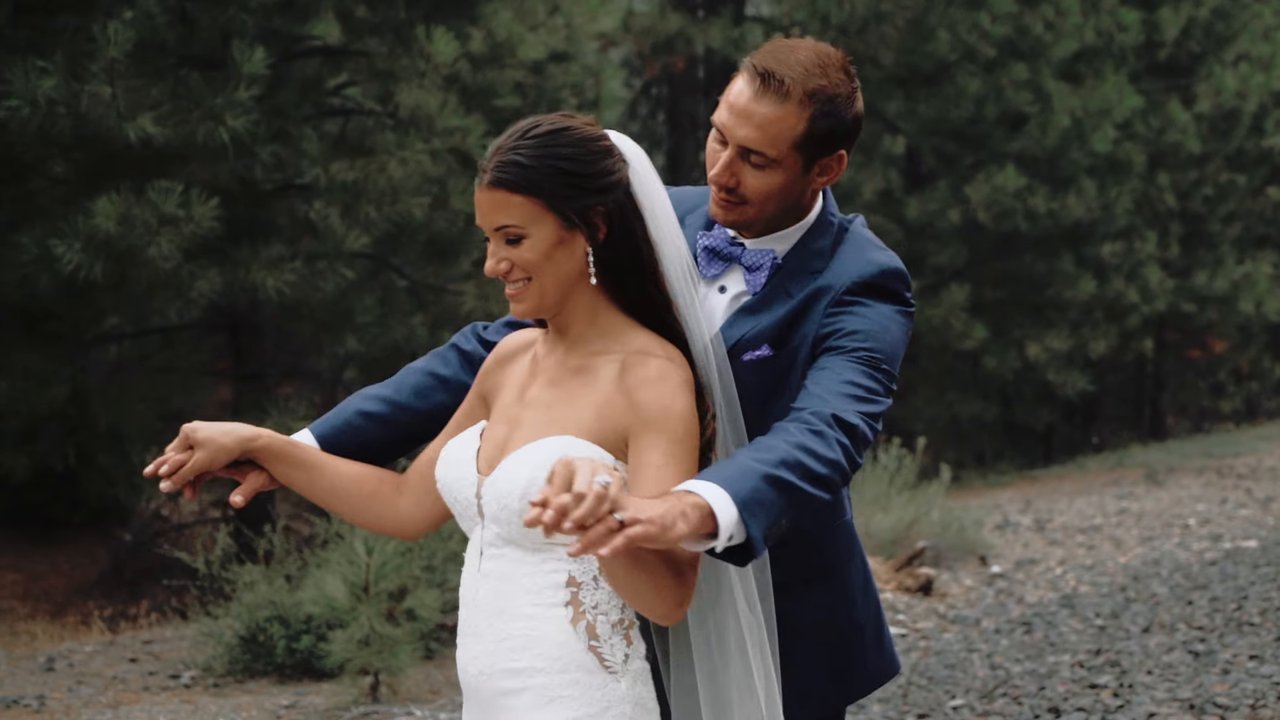 Wes hugs Jen from behind as she laughs among the pines