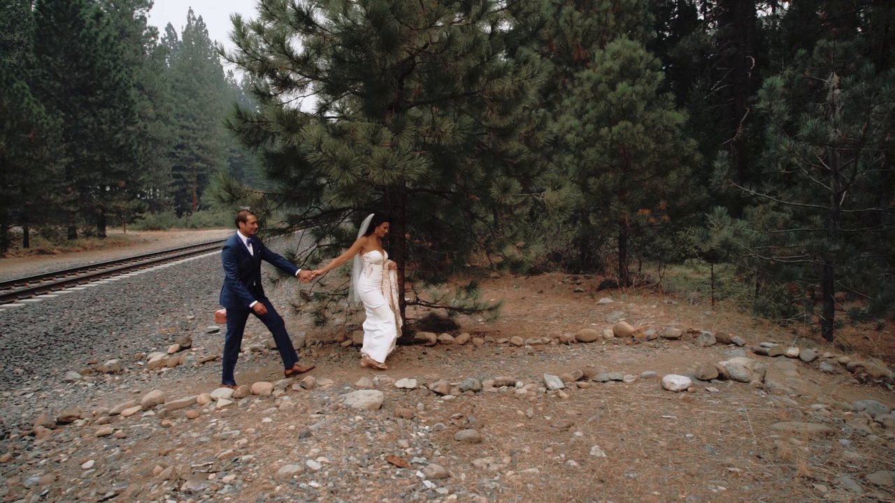 Wes leads Jen by the hand beside the railroad tracks