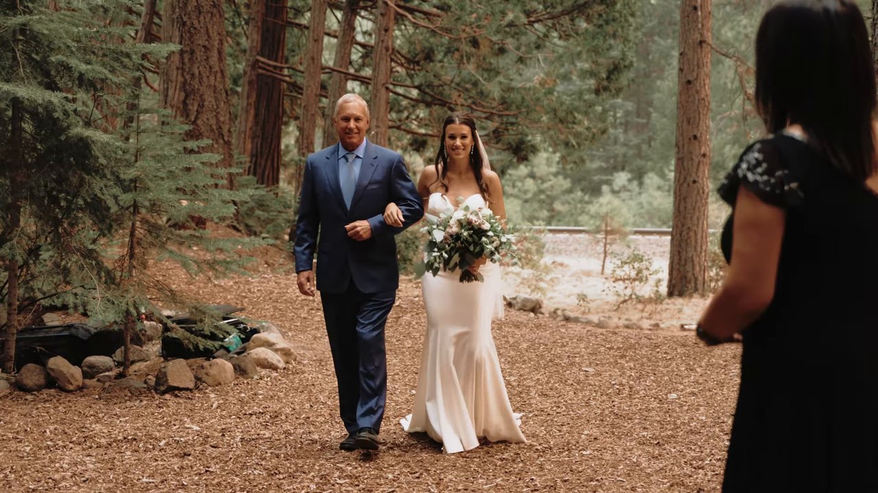 Jen walks down the forest aisle on her dad's arm holding her bouquet