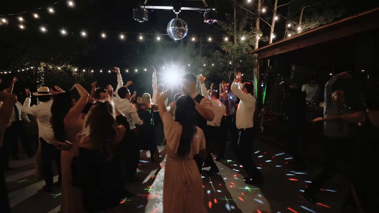 Guests with their hands in the air on a packed dance floor under the mirror ball and string lights