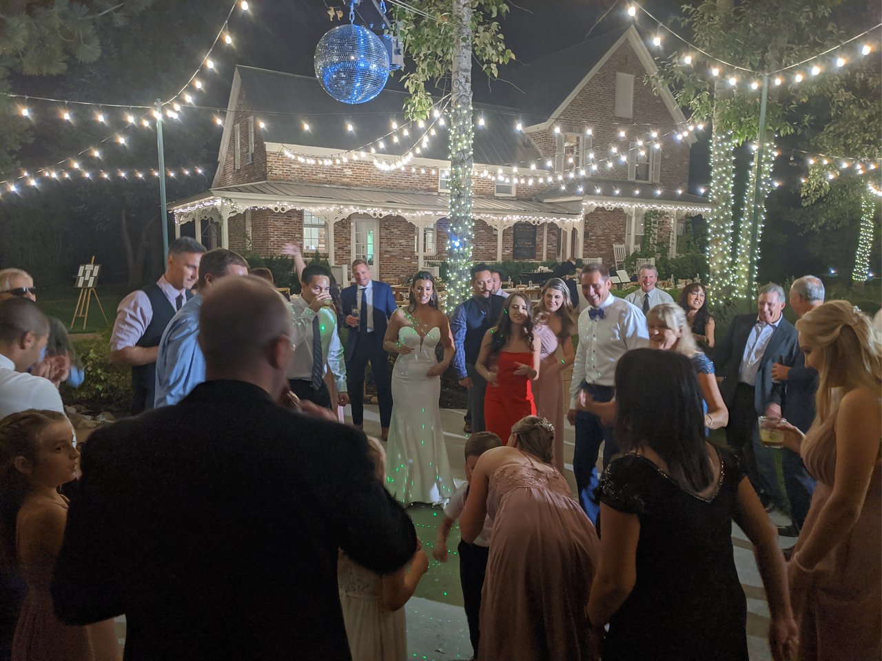 Jen dances in the middle of a crowded dance floor under a mirror ball and string lights in front of the brick house