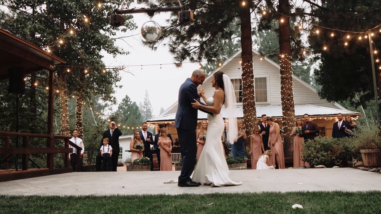 Jen dances with her dad on the patio under string lights and a mirror ball