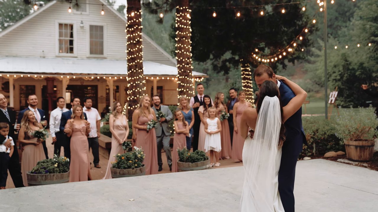 Jen and Wes share their first dance on the patio as the wedding party watches under string lights