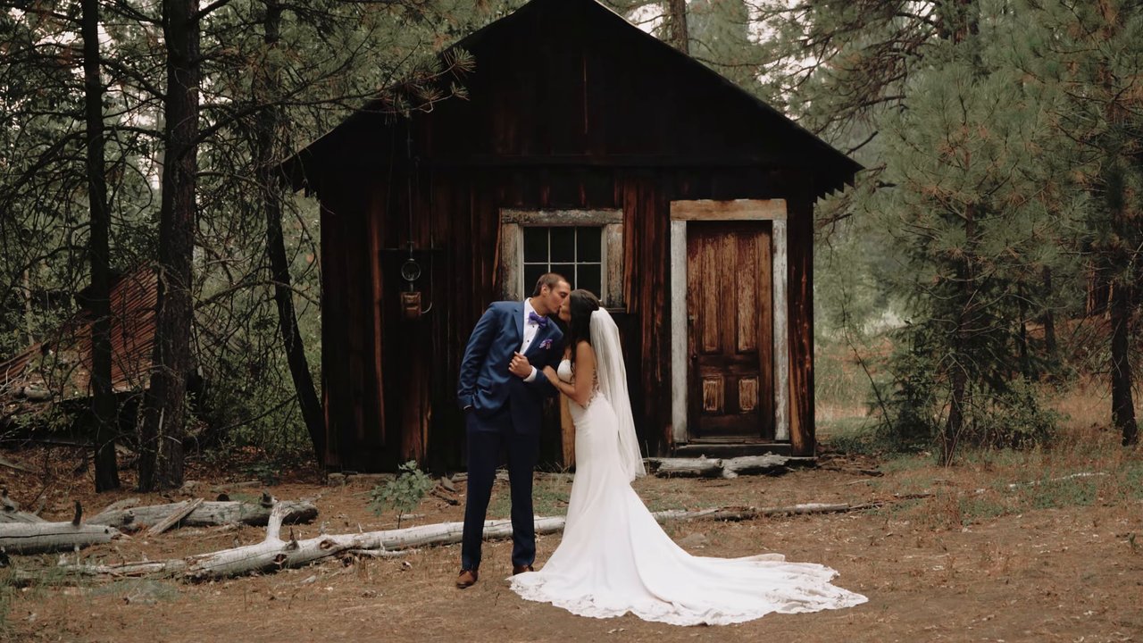 Jen and Wes share a kiss in front of an old wooden cabin in the pines before the ceremony