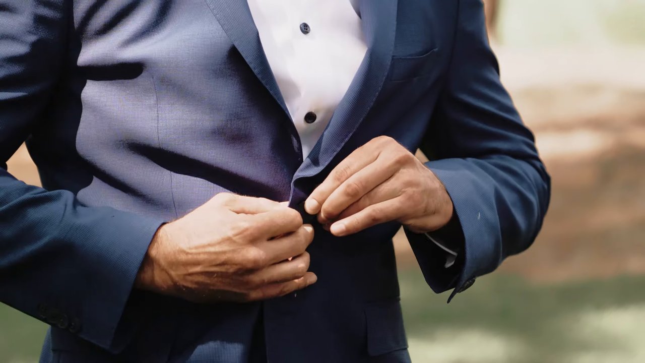A groomsman buttons his navy jacket