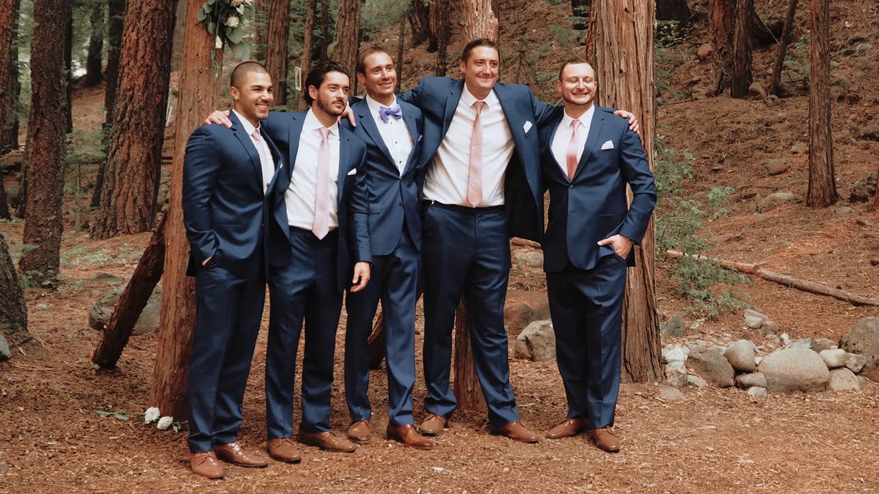Wes and his groomsmen in navy suits stand arm in arm in the forest