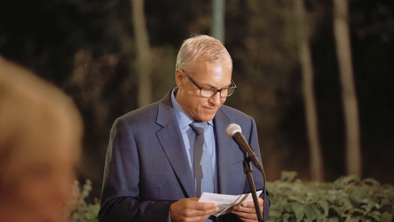 A guest in a gray suit reads his toast at the microphone