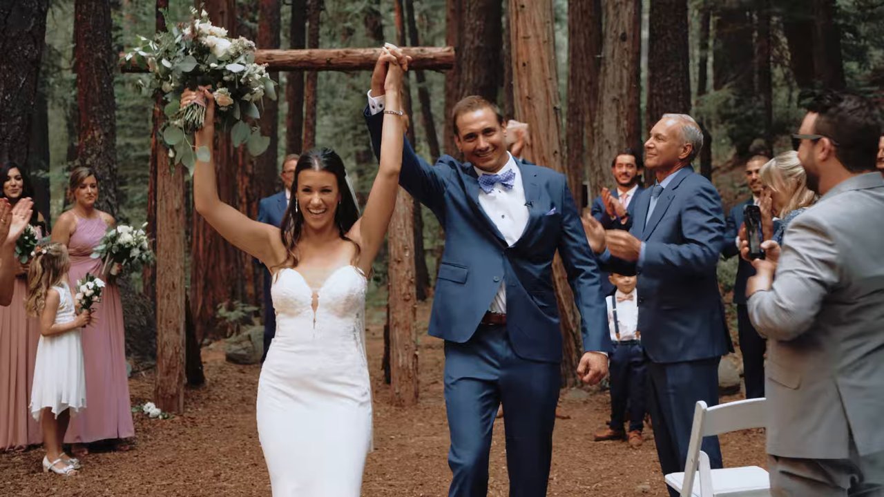Jen and Wes raise their joined hands in a cheer as they walk back up the aisle as husband and wife