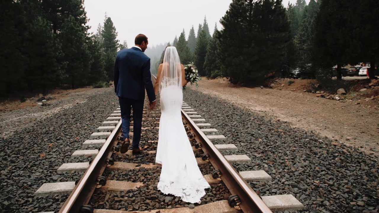 Jen and Wes walk away down the railroad tracks into the pines