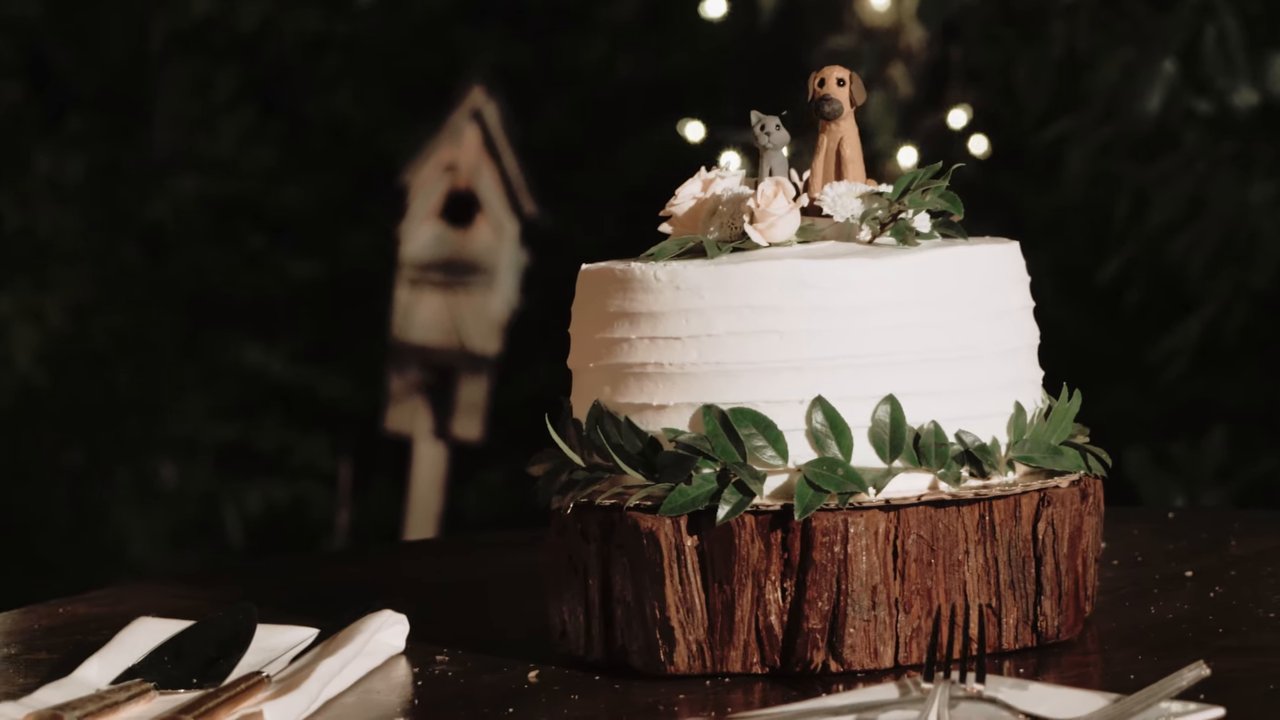 The white wedding cake with a dog cake topper on a wood slice