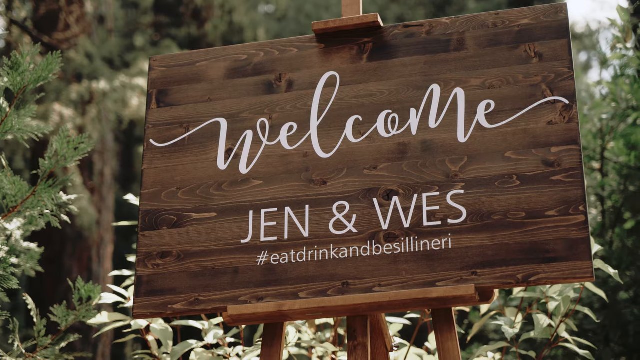 A wooden welcome sign for Jen and Wes among the ferns